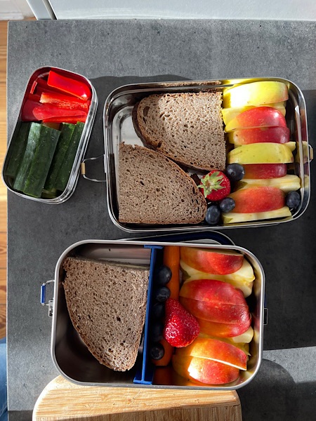 Edelstahl-Brotboxen, gefüllt mit Broten, Apfel, Karotte, Gurke, Paprika, Karotte und Blaubeeren.