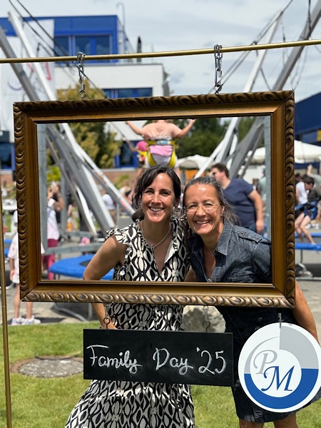 Ingrid Holscher und Petra Büeler lächeln beim Family Day von PM International durch einen Foto-Bilderrahmen. Im Hintergrund ist das Trampolin für die Kinder zu sehen.