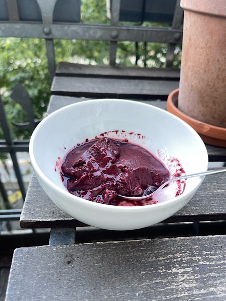 Selbstgemachtes Blaubeer-Sojaghurt Eis in weißer Porzellanschale auf Balkontisch