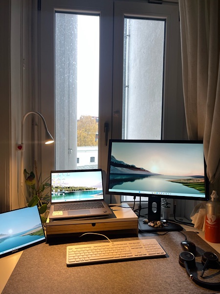 Homeoffice Platz mit drei angeschalteten Bildschirmen vor einem Fenster